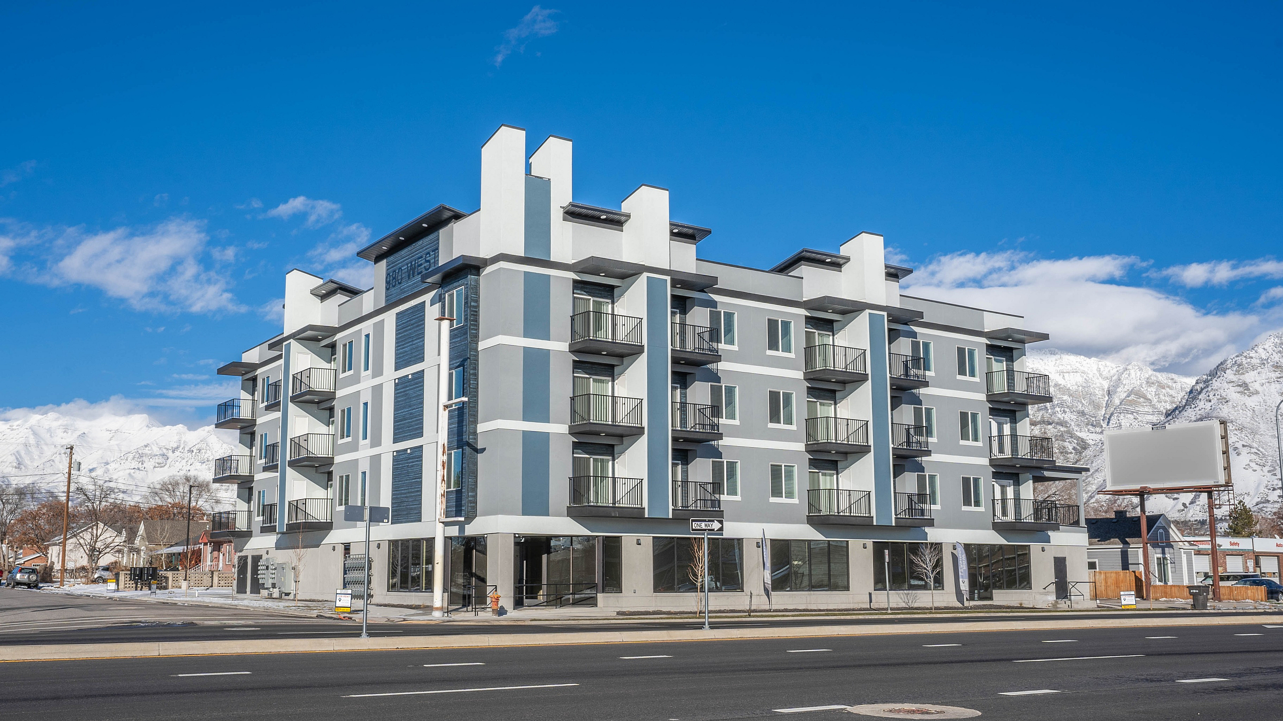 Modern apartment building with stylish balconies set against a backdrop of scenic snow-capped mountains and clear blue skies.