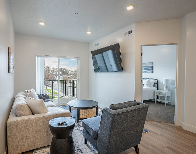 Cozy living room with a plush sofa, modern decor, and a large wall-mounted TV, offering a bright, inviting atmosphere with balcony views.
