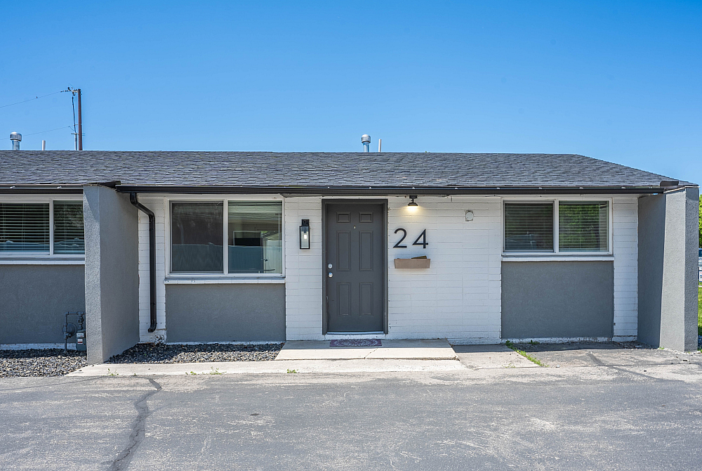 Charming duplex exterior with modern grey accents, featuring large windows and a welcoming front door under a clear blue sky.
