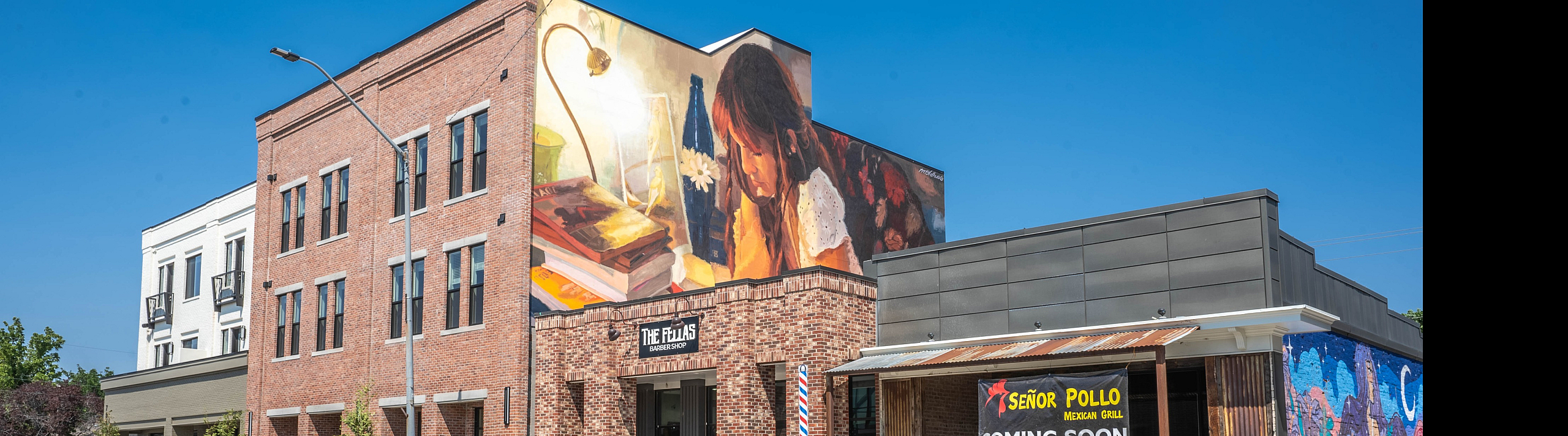 Charming urban scene featuring a lively Mexican grill coming soon, vibrant murals, and a rustic brick barber shop.