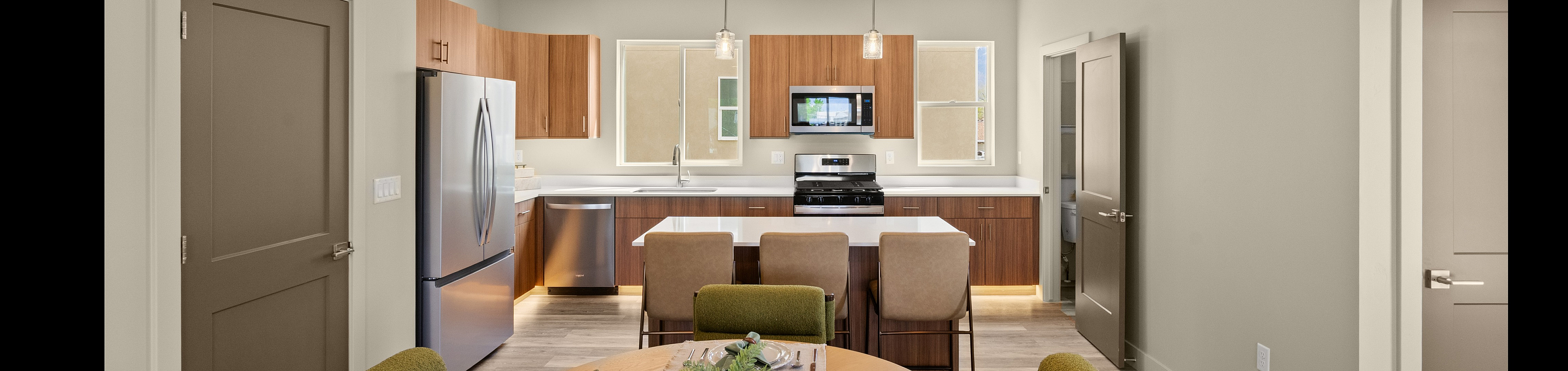 Modern kitchen and dining area with sleek cabinetry, stainless steel appliances, and elegant lighting. Cozy dining table set for four with green accents.