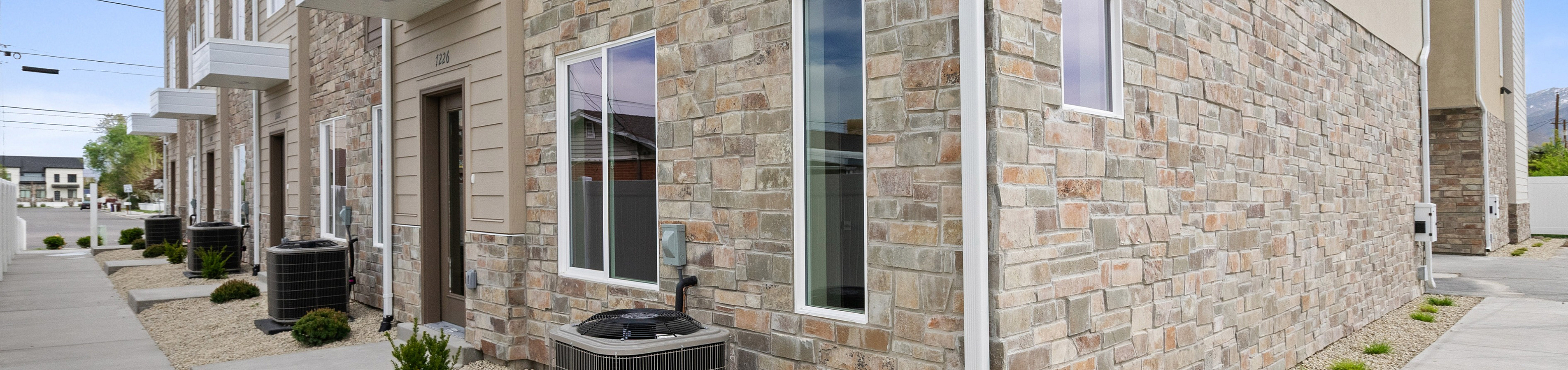 Contemporary townhouse exterior with elegant stone facade, modern windows, and sleek landscaping in a vibrant neighborhood.