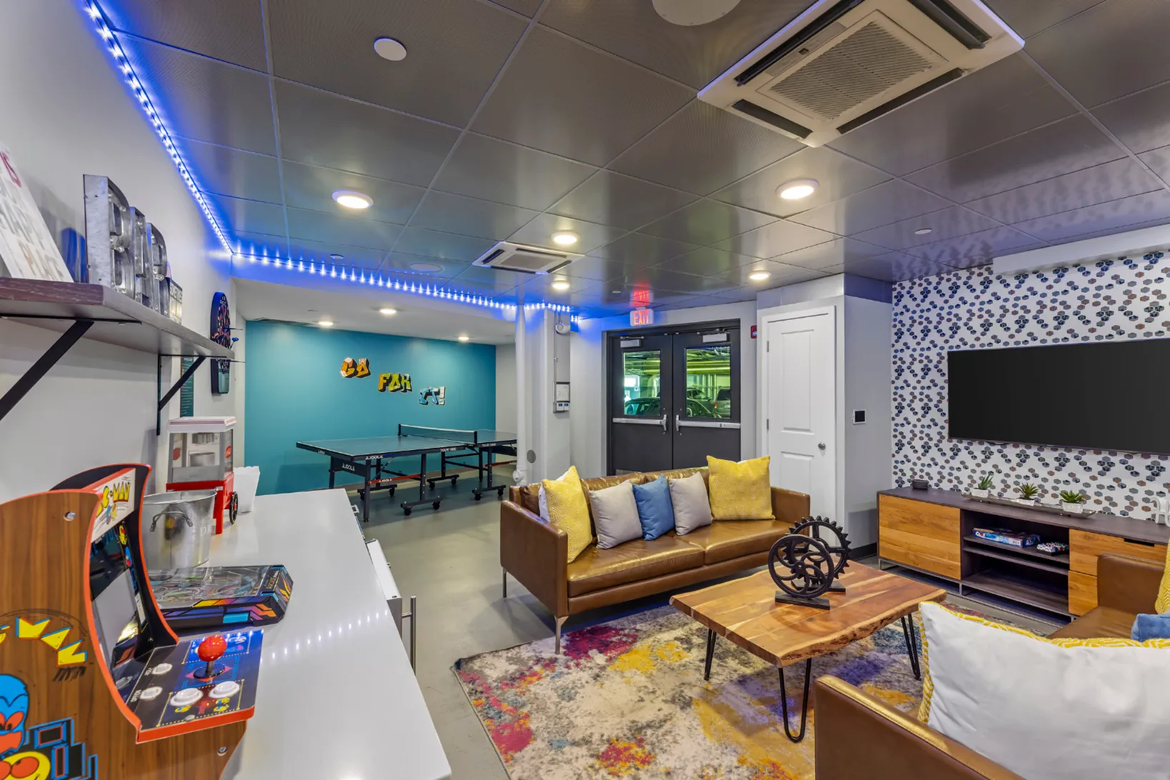 Modern entertainment room featuring a cozy seating area, vibrant rug, stylish decor, ping-pong table, and vintage arcade game.