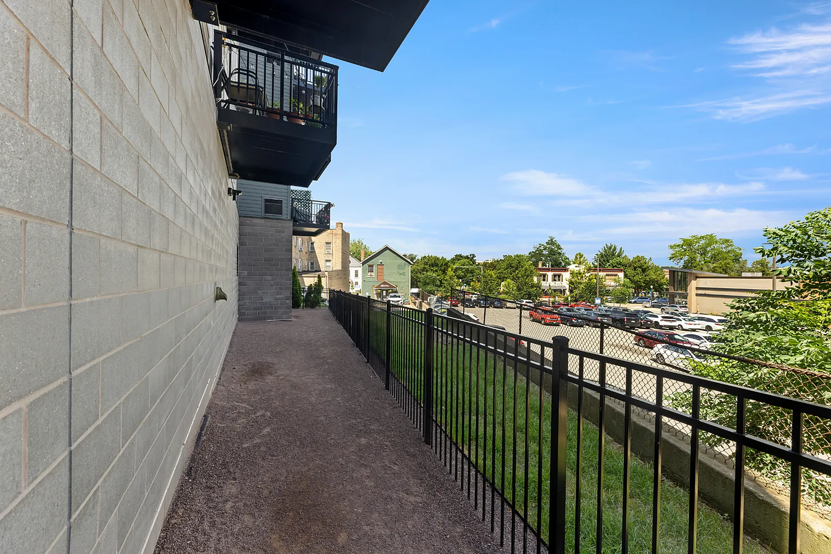Charming urban balcony view with contemporary railing overlooking a sunlit neighborhood and lush trees.