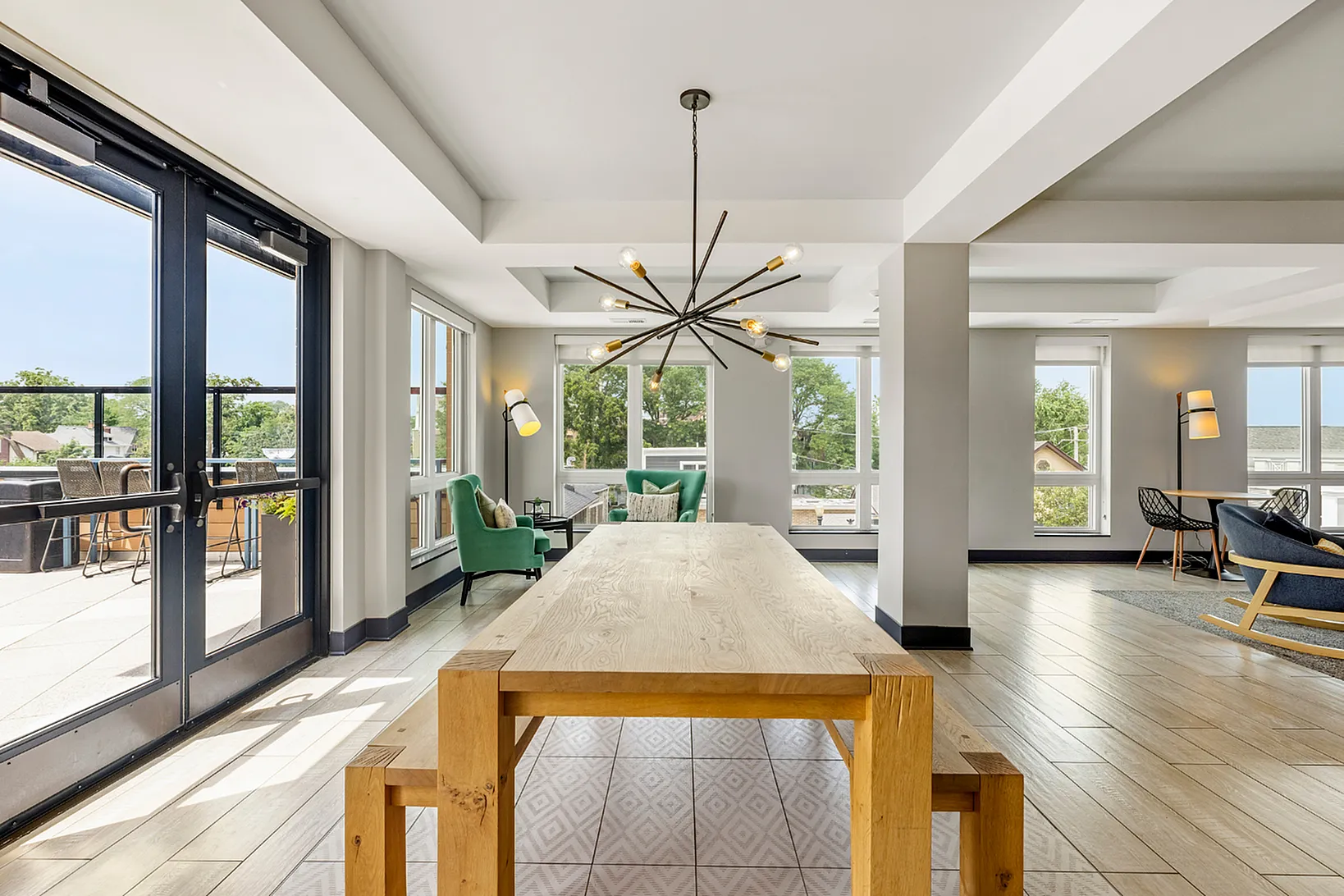 Bright and inviting modern apartment interior with large windows, elegant chandelier, and cozy seating area overlooking a spacious balcony.