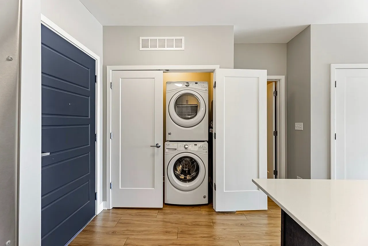 Modern apartment with sleek laundry area featuring a stacked washer and dryer tucked into a stylish closet with crisp white doors.