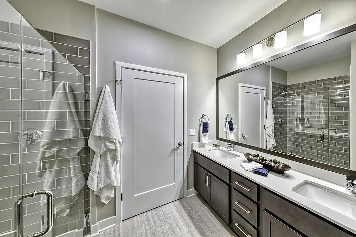 Elegant modern bathroom featuring double vanity, sleek mirrors, and a spacious glass shower with gray tile accents.