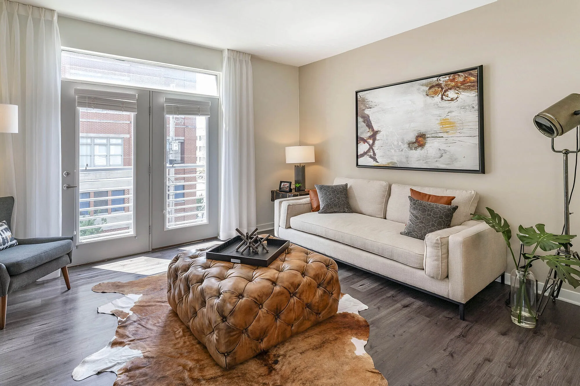 Elegant contemporary living room featuring a plush cream sofa, artistic wall decor, and natural light streaming through large French doors.