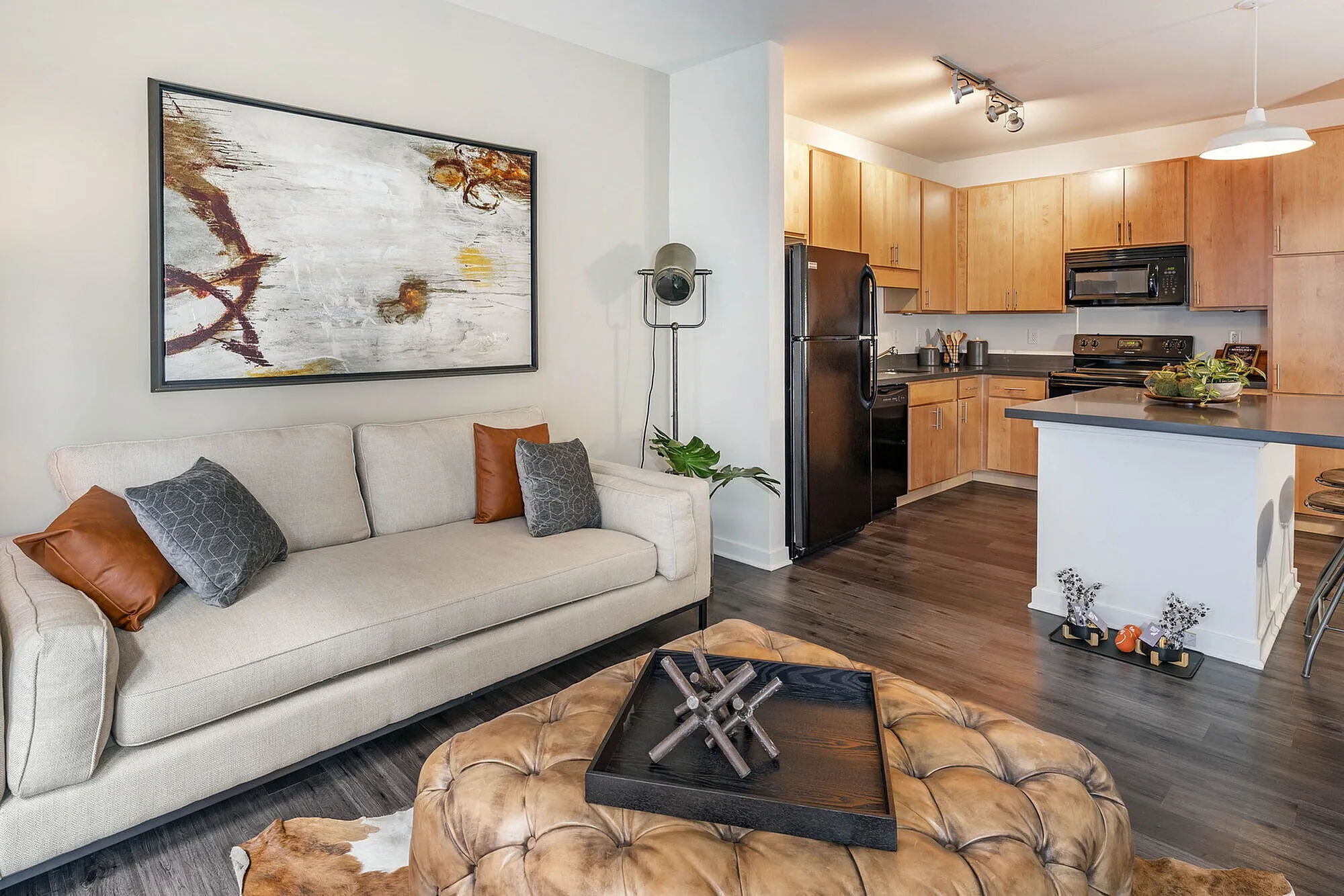 Modern living space featuring a cozy beige sofa, stylish artwork, and an inviting open-concept kitchen with warm wooden cabinets and sleek black appliances.