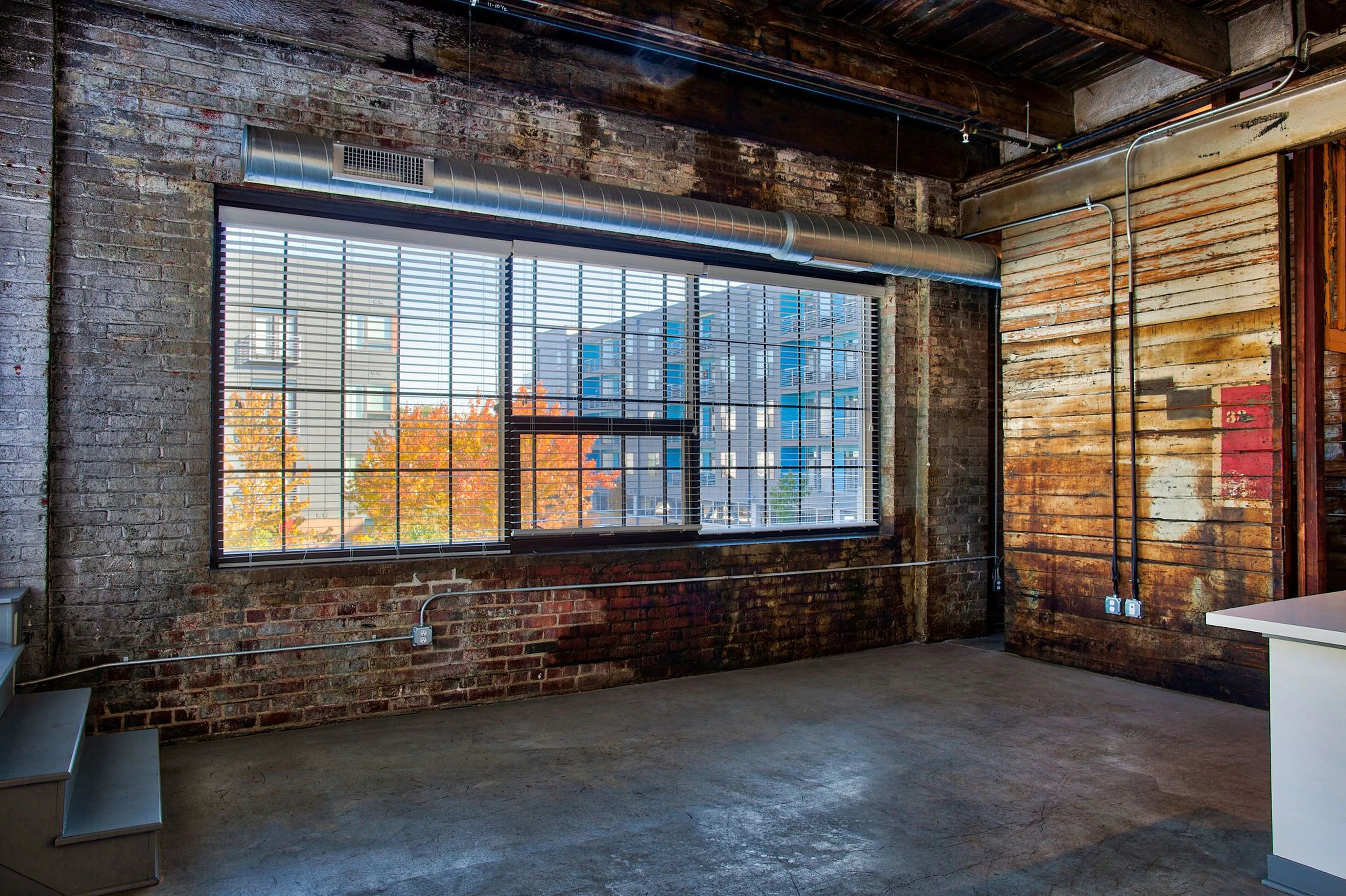 Chic industrial loft featuring exposed brick walls, large windows with city views, and rustic wooden elements.