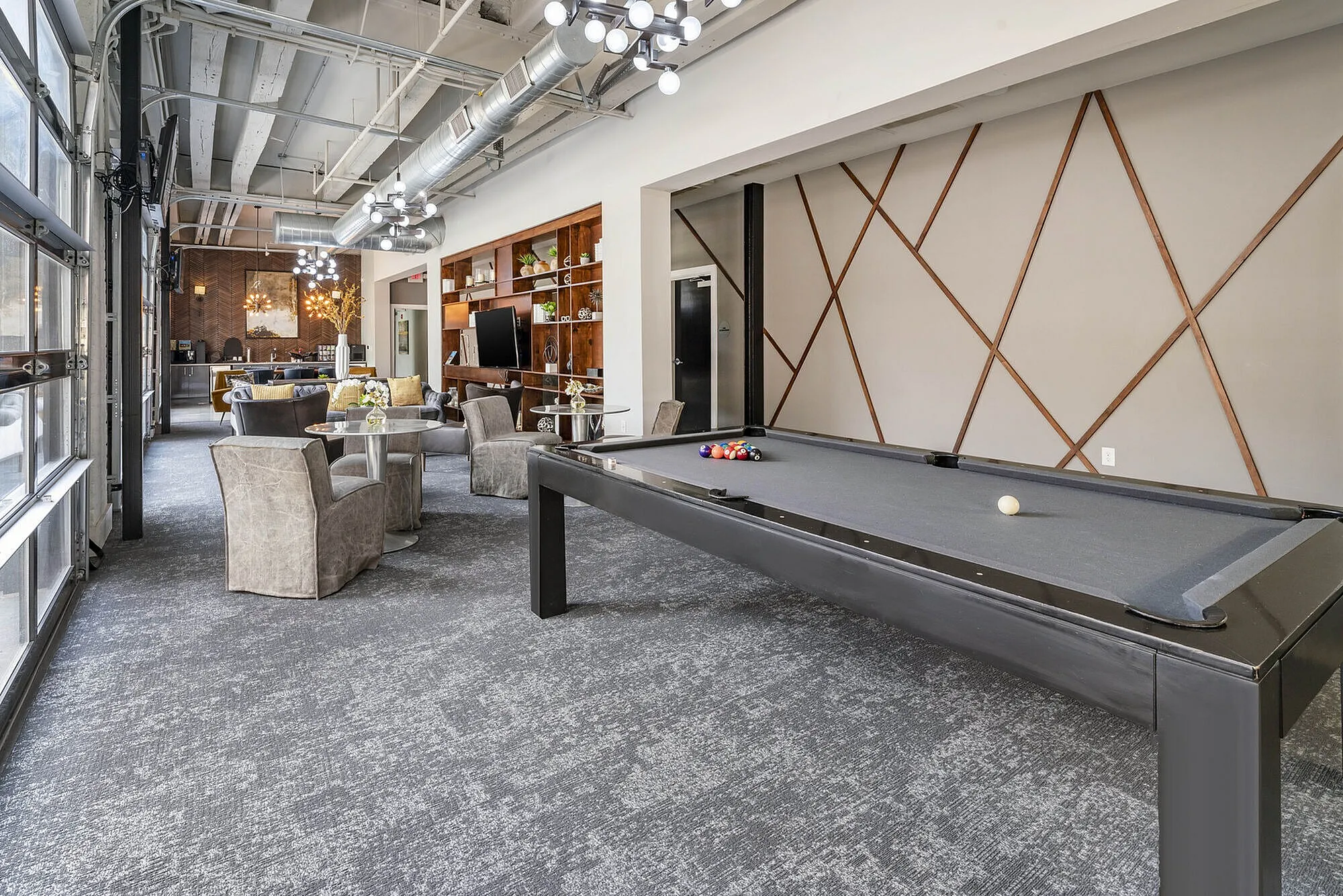 Modern lounge area with elegant pool table, stylish seating, and contemporary lighting in a bright, spacious setting.