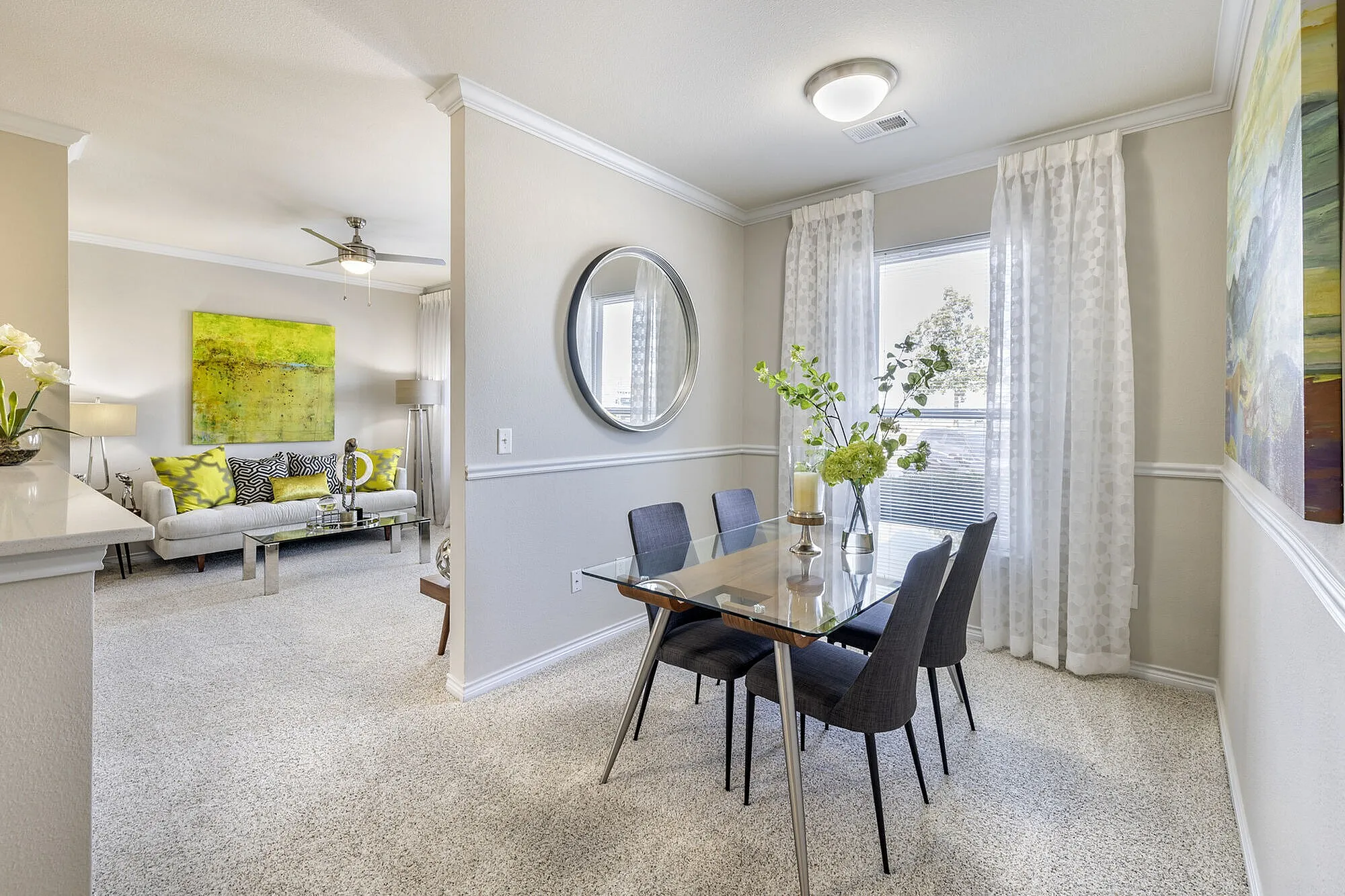 Bright and elegant dining area with a modern glass table and chic decor leading to a cozy, inviting living room with stylish accents.