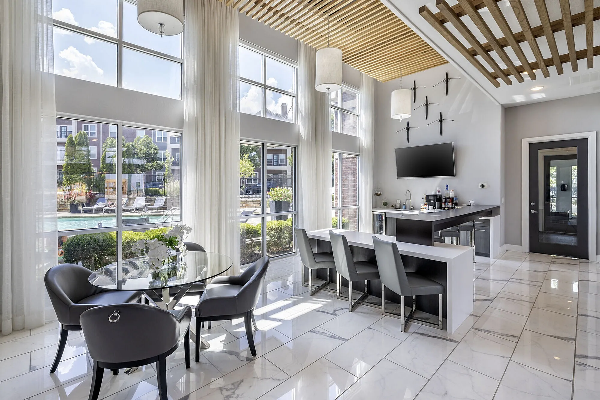 Bright, modern lounge area with floor-to-ceiling windows, sleek seating, and chic decor boasting views of a poolside outdoor space.