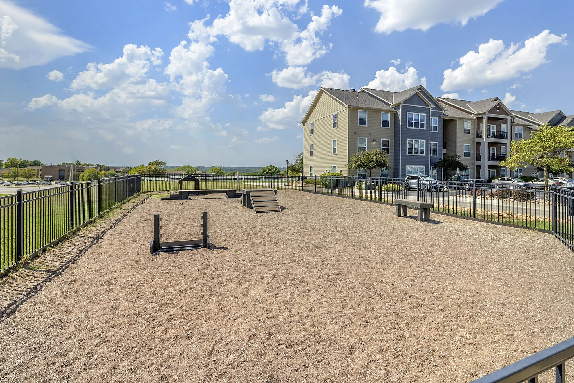 Pet-friendly apartment complex featuring a spacious fenced dog park with agility equipment and stunning blue skies.