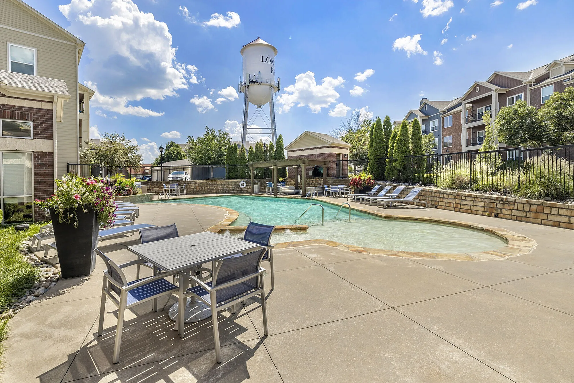 Inviting outdoor pool area at a stylish apartment complex, featuring comfortable lounge chairs and vibrant landscaping under a clear blue sky.