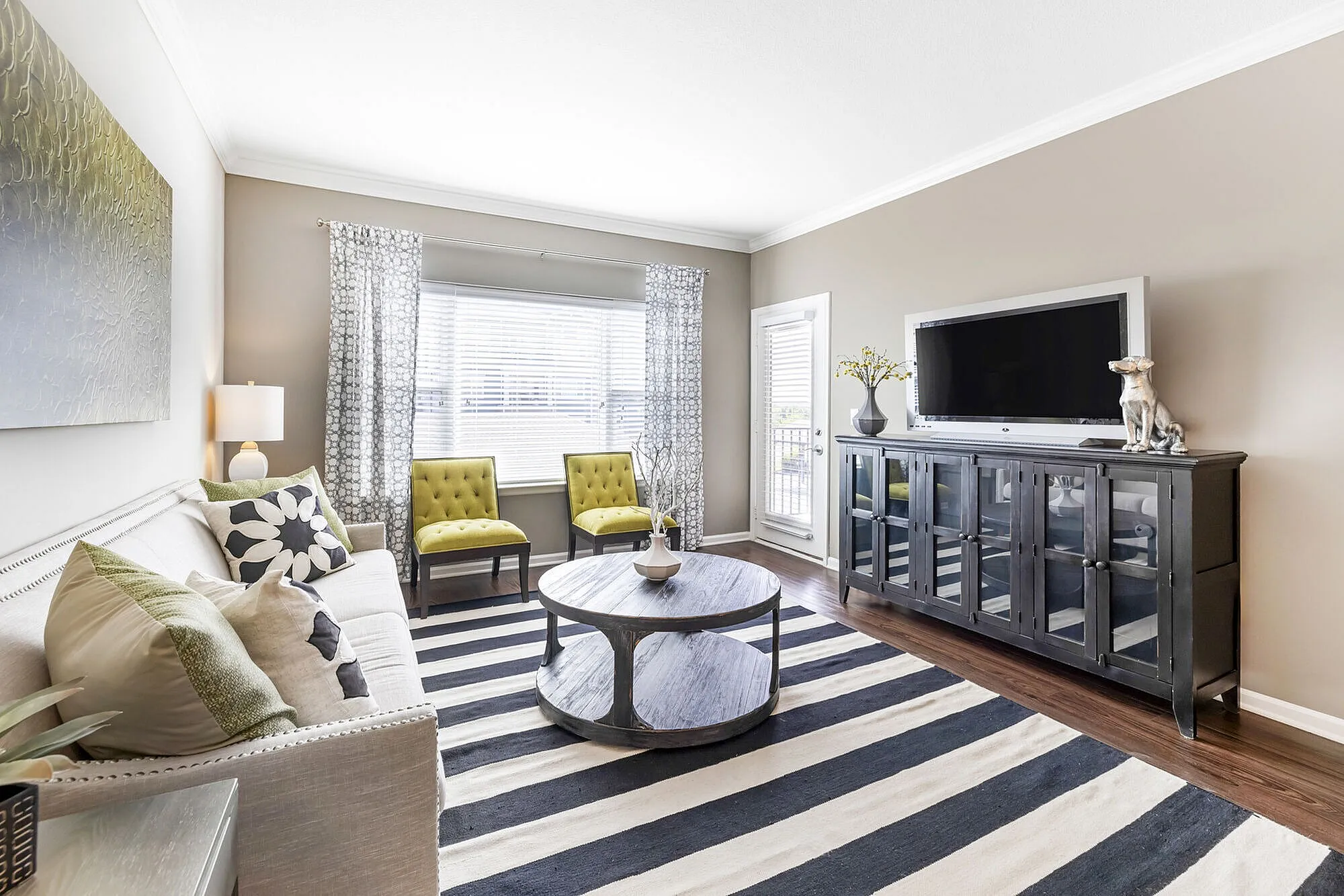 Elegant living room with natural light, chic striped rug, stylish sofa, and vibrant green accent chairs.