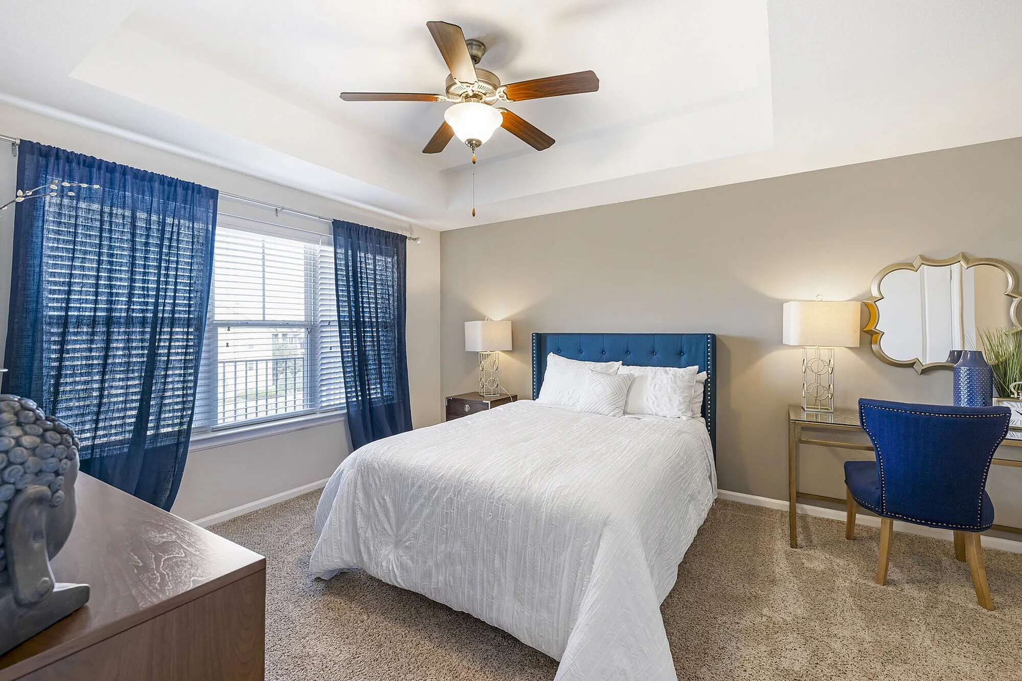 Bright and inviting bedroom with elegant decor, featuring a cozy bed, stylish blue accents, and natural light filtering through large windows.