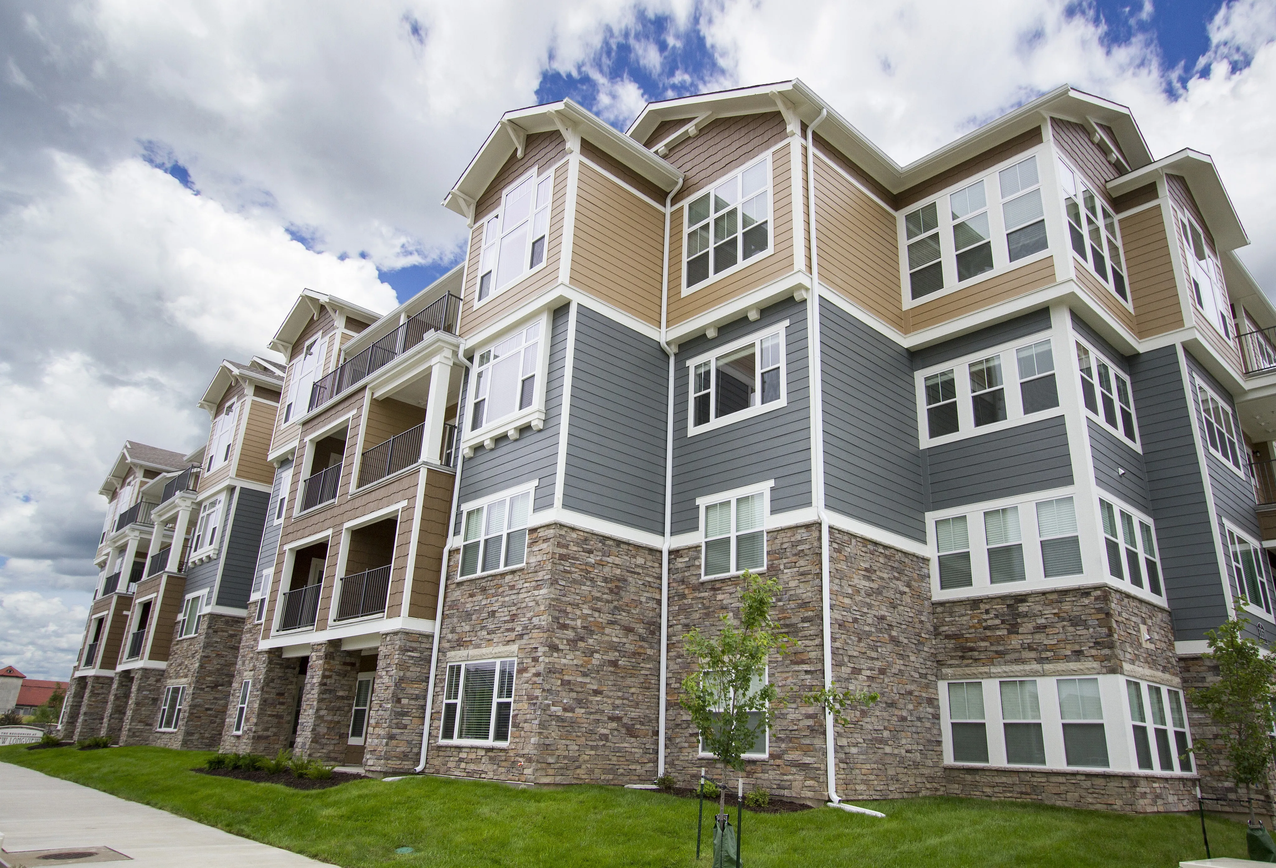 Modern apartment complex with appealing stone and siding exterior, showcasing spacious balconies and large windows against a clear sky.