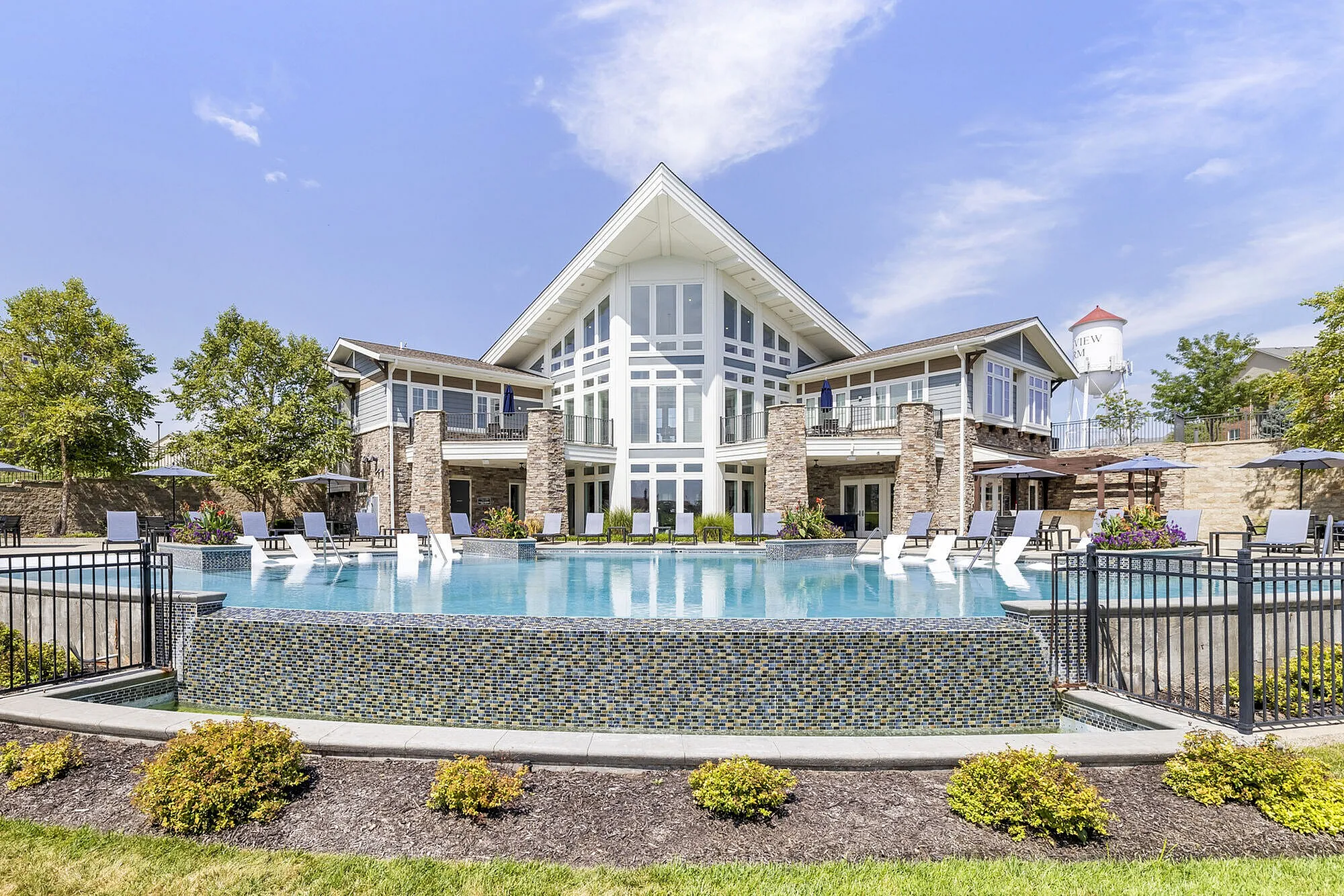 Luxurious apartment complex with a stunning outdoor pool, elegant stone facade, and modern design elements under a clear blue sky.