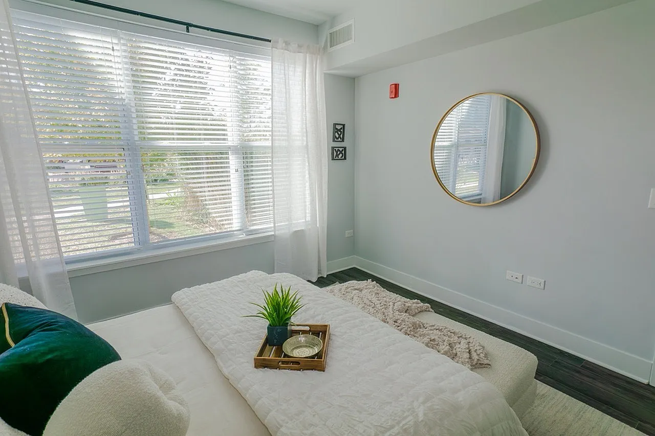 Bright and cozy bedroom with large windows, stylish decor, and a minimalist mirror, offering a tranquil retreat with plenty of natural light.