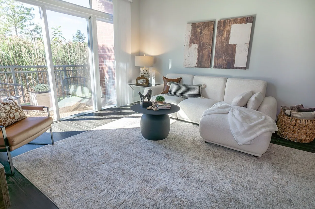 Inviting living room with modern decor, cozy white sofa, and abundant natural light through large glass doors opening to a serene balcony view.