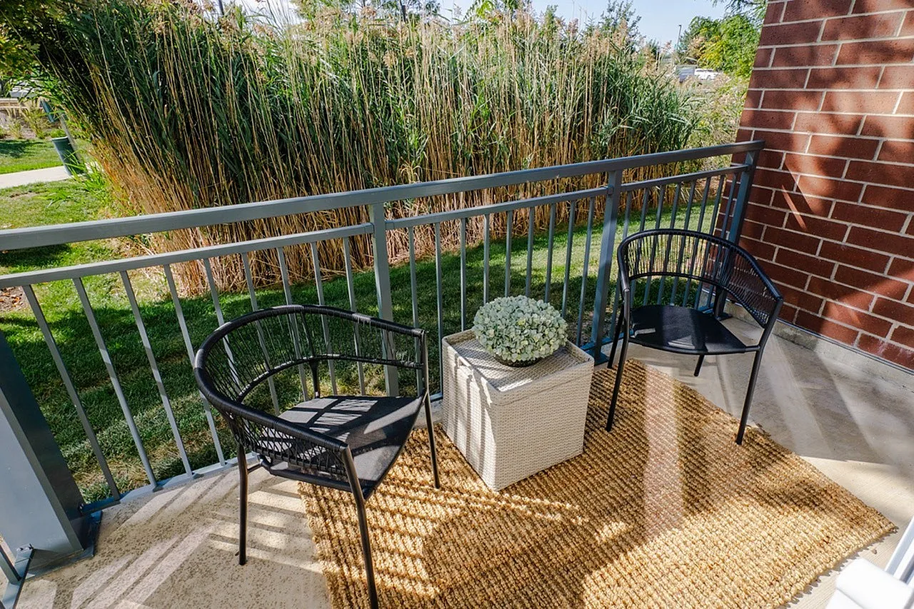 Charming apartment balcony with modern black chairs, a woven rug, and lush greenery views.