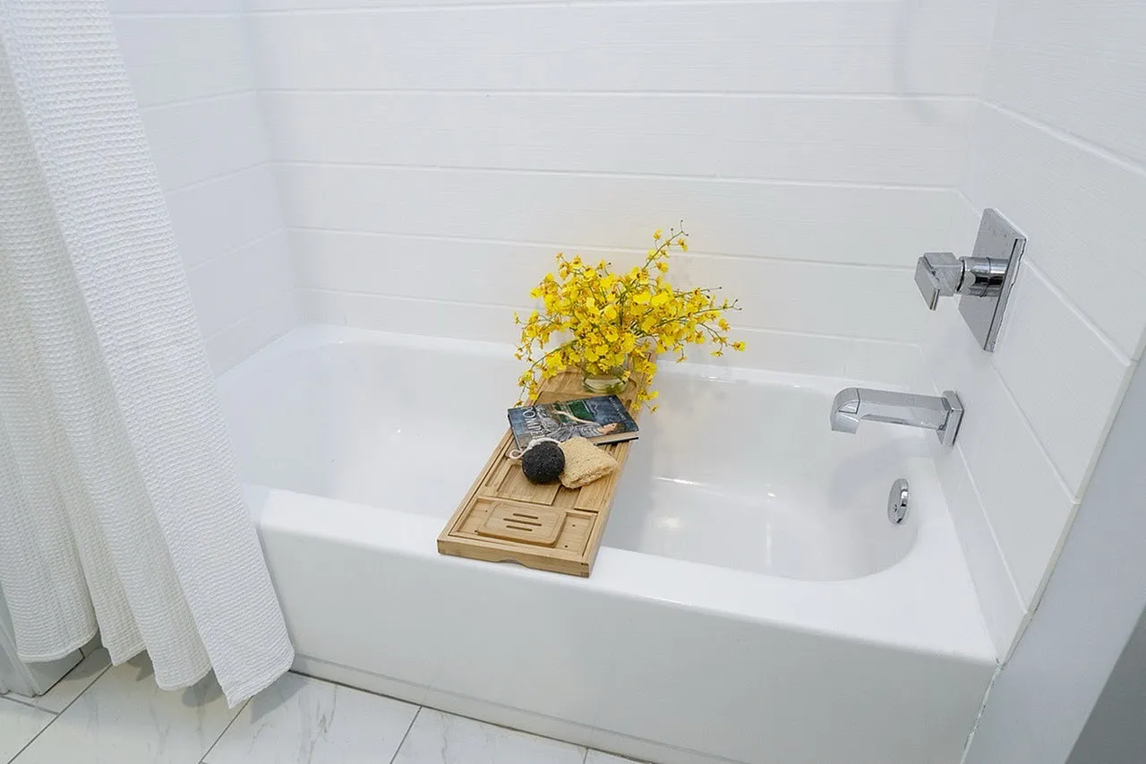 Elegant bathroom featuring a pristine white bathtub with a luxurious wooden bath tray, accented by vibrant yellow flowers and spa essentials for a relaxing atmosphere.
