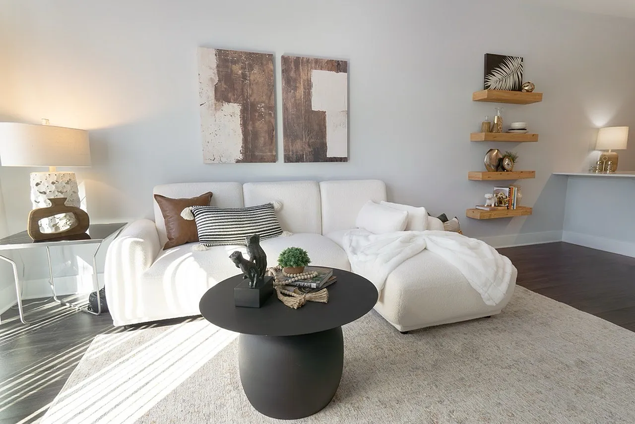 Elegant living room showcasing a plush white sectional, chic artwork, and stylish shelves with decorative accents creating a cozy, inviting ambiance.