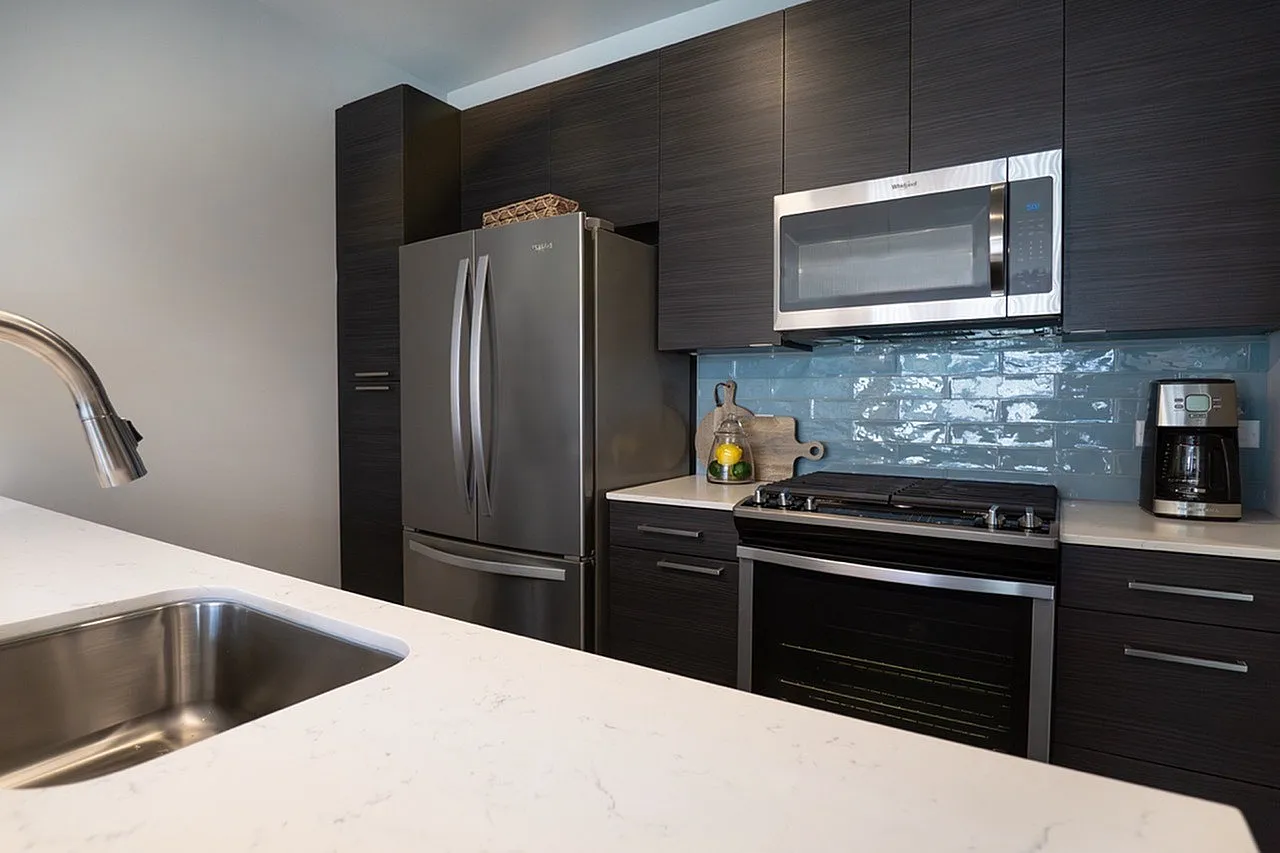 Modern kitchen with sleek stainless steel appliances, elegant dark cabinetry, and a stylish blue tile backsplash.