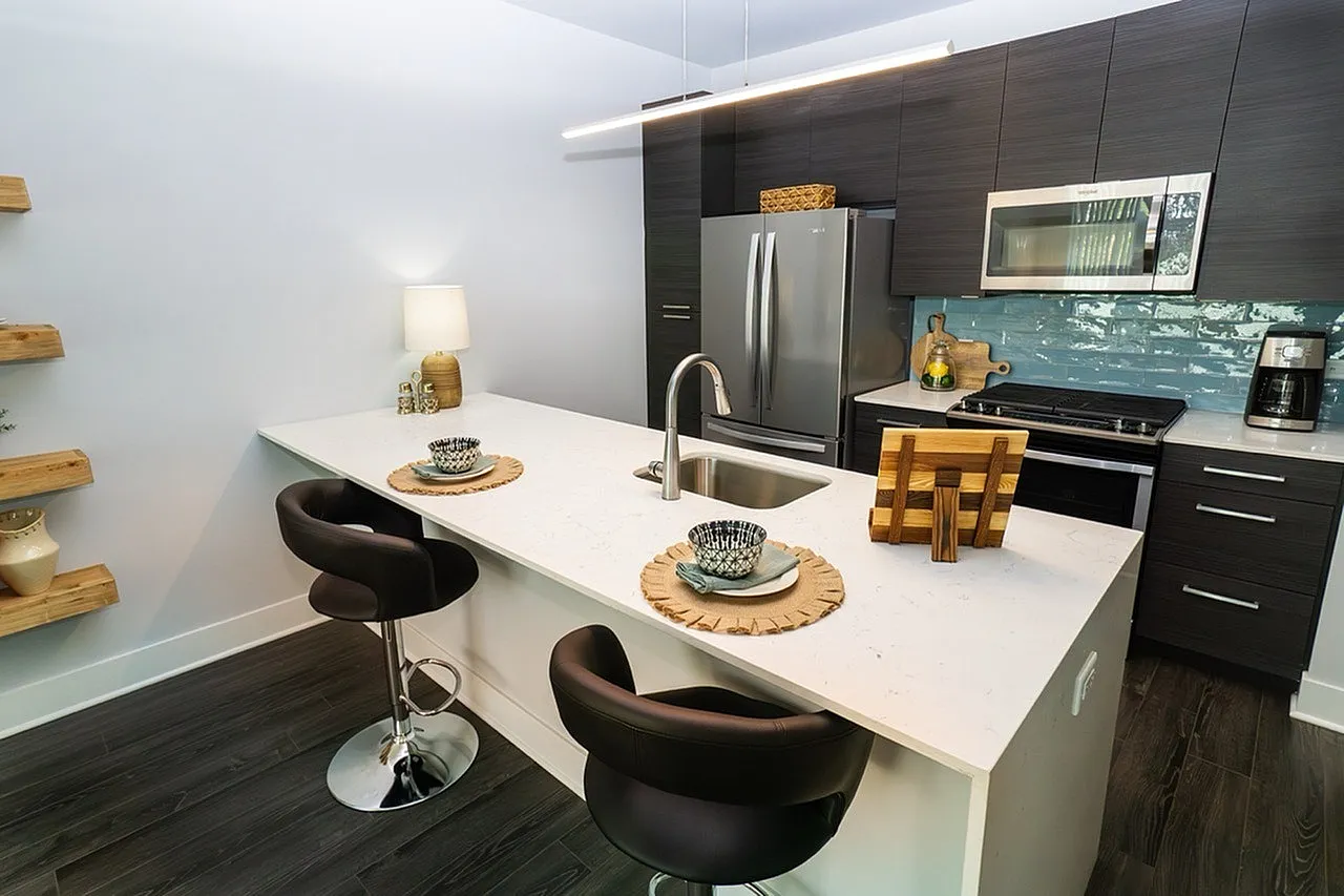 Modern kitchen with sleek dark cabinets, stainless steel appliances, and a spacious white countertop featuring stylish bar seating.