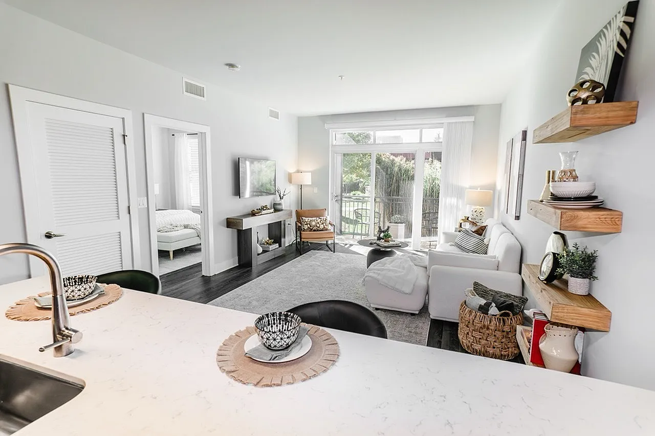 Bright, contemporary open-plan living room with stylish decor, featuring a cozy seating area, modern kitchen space, and a view of the lush garden through large sliding doors.