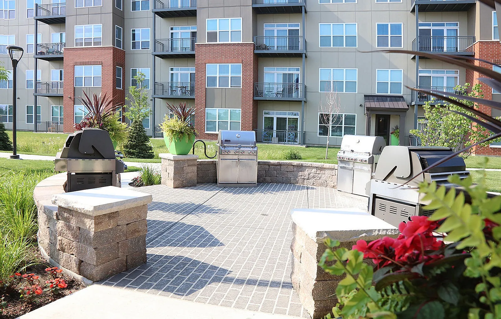 Modern apartment exterior with stylish balconies, landscaped greenery, and a communal grilling area.