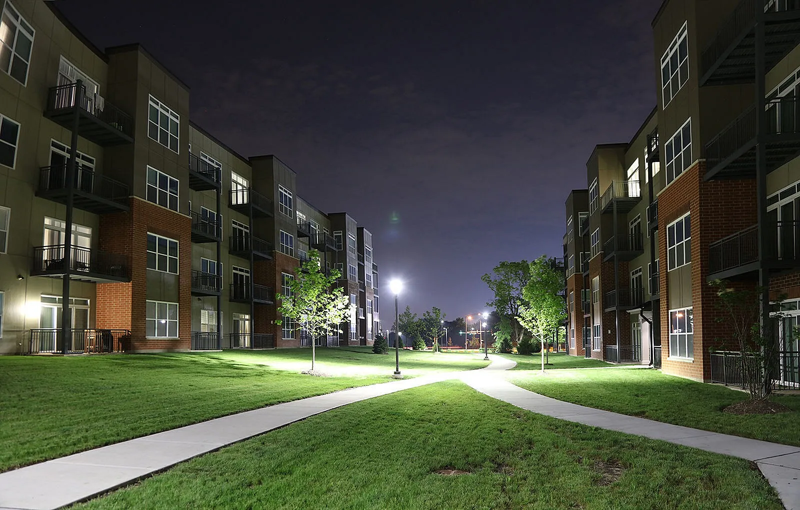 Elegant apartment complex with modern design, illuminated at night, featuring well-maintained green spaces and pathways, offering a serene and upscale living environment.