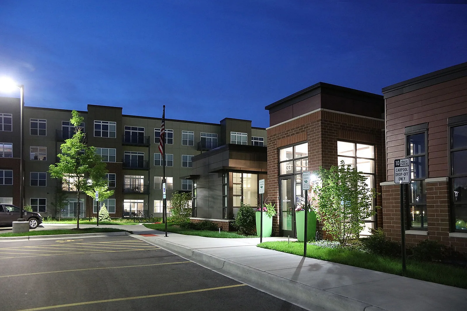 Elegant apartment complex exterior at night, featuring modern architecture and warm lighting, highlighting lush landscaping and ample parking.