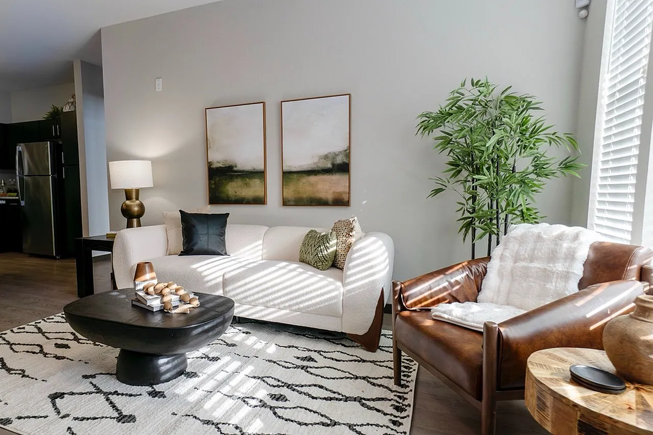 Chic living room boasting a modern white sofa, elegant leather chair, tasteful artwork, and lush greenery, bathed in natural light.