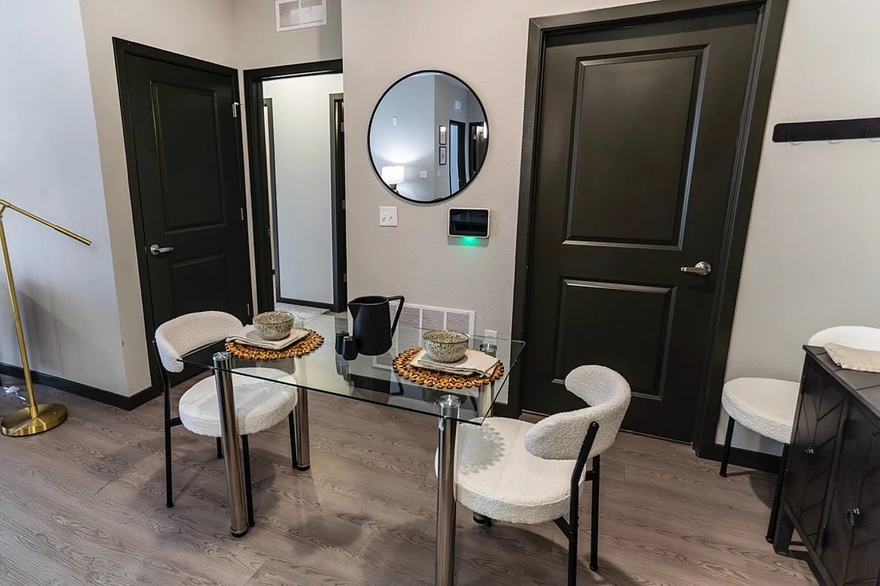 Chic dining area with elegant glass table and modern decor, highlighted by cozy seating and stylish black doors.