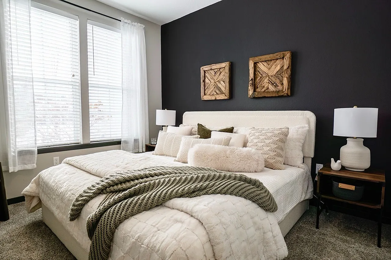 Elegant bedroom featuring a stylish bed with plush pillows, modern lamps, and artistic wooden wall decor.