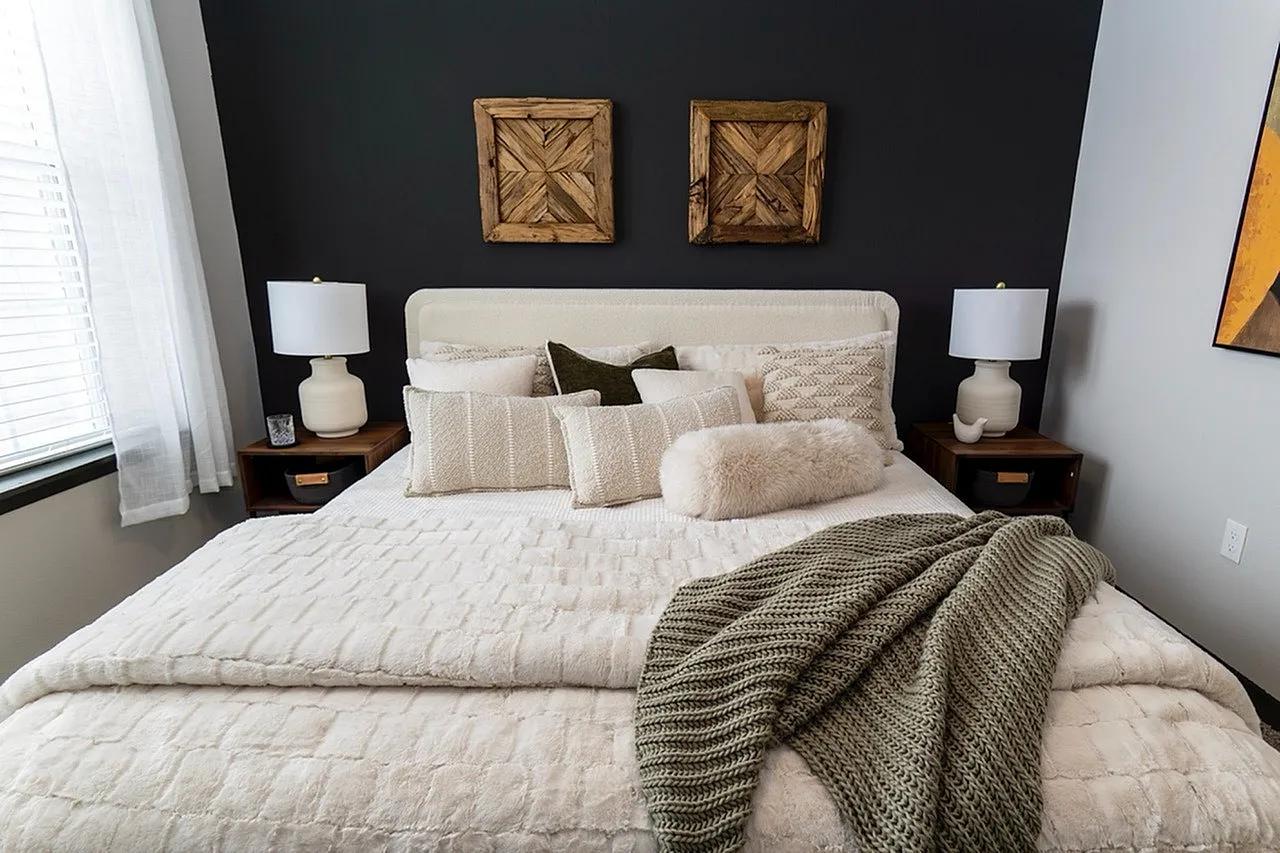 Inviting bedroom with a luxurious king-sized bed, plush pillows, and a cozy knit blanket, enhanced by warm lighting and rustic wall decor.
