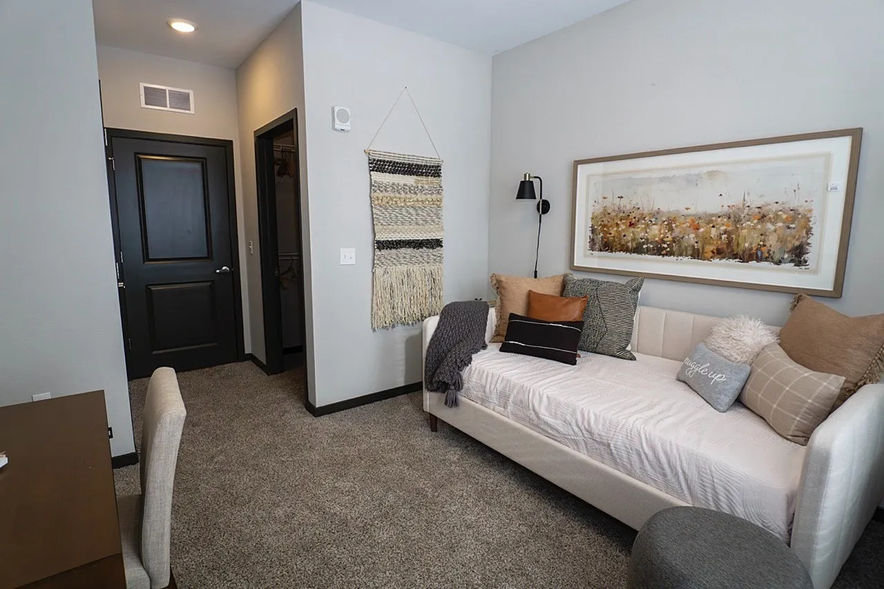 Chic apartment bedroom with cozy daybed, plush pillows, modern artwork, and a stylish woven wall hanging.