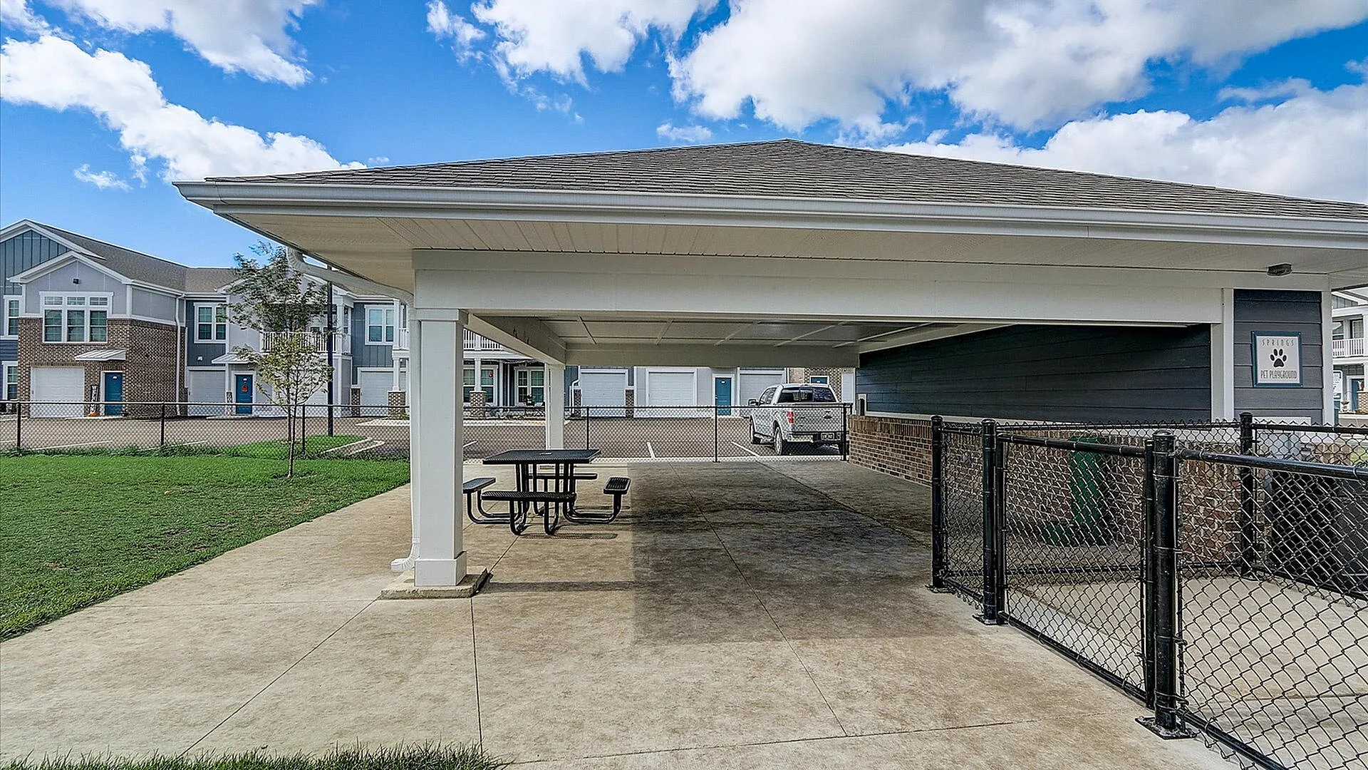 Inviting apartment complex showcasing outdoor picnic area and ample parking space, set against a blue sky with modern architecture.