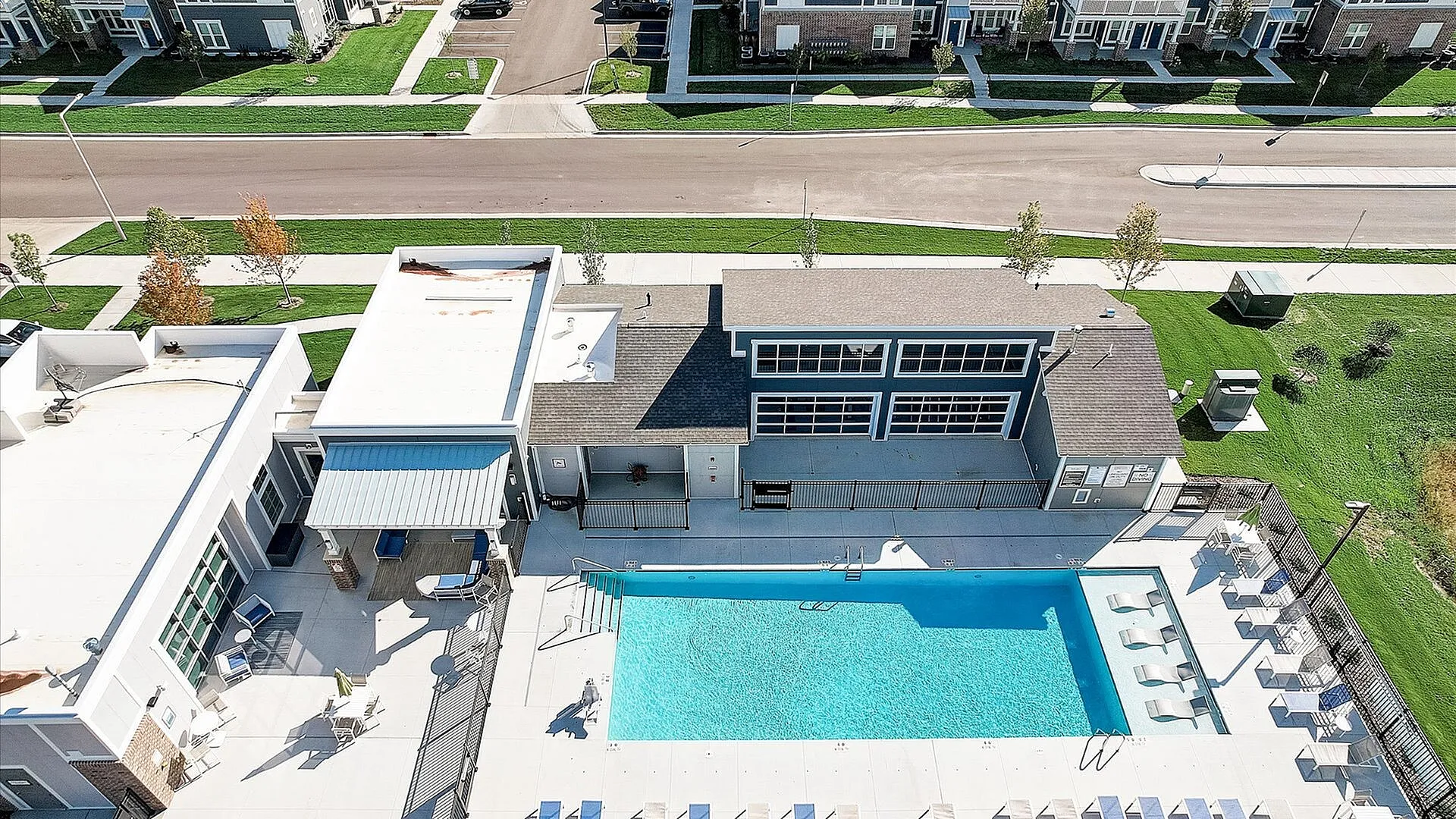 Aerial view of a modern residential complex featuring a sparkling blue pool, stylish lounge area, and surrounding green lawns.