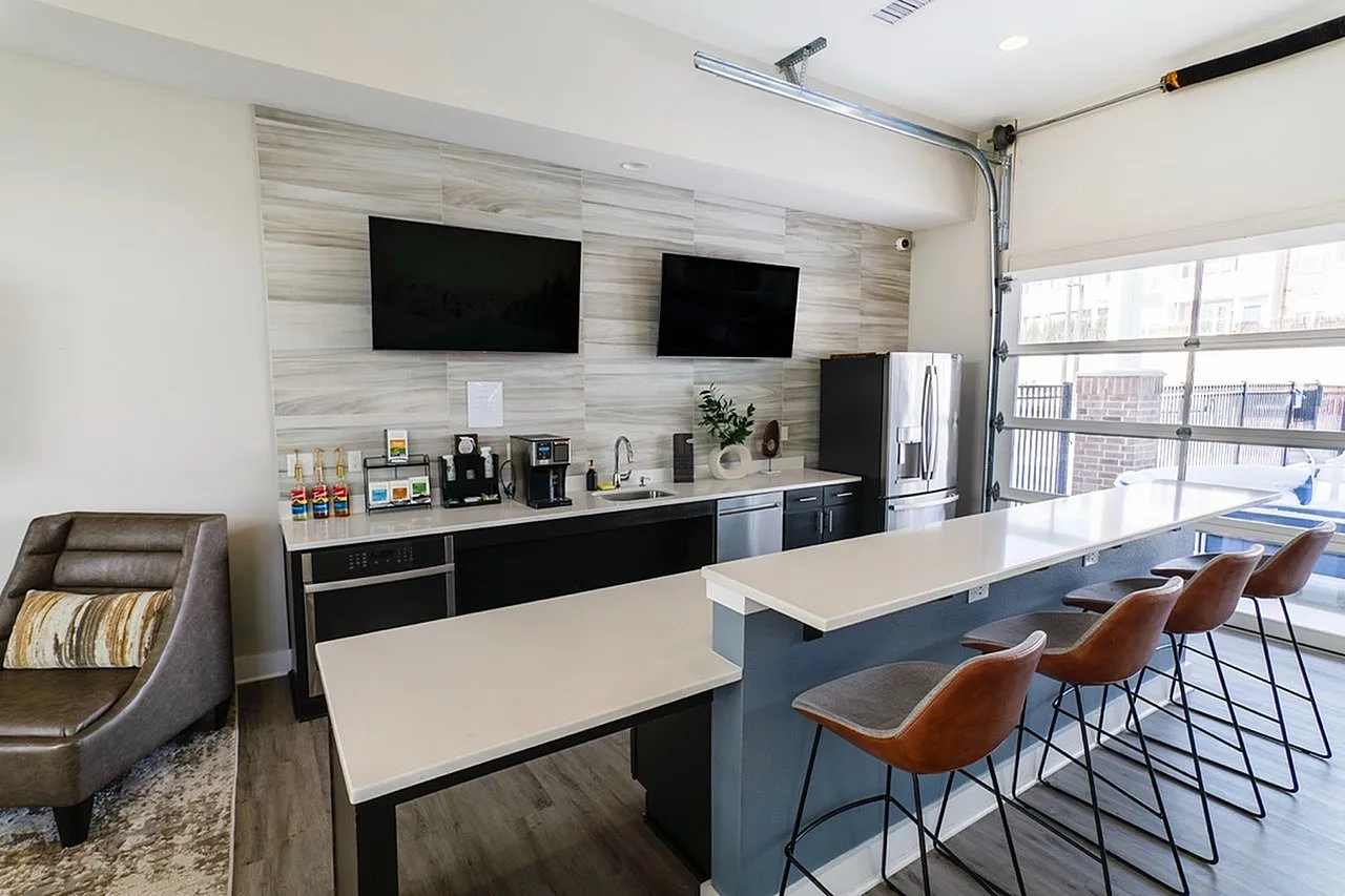 Modern kitchen space with sleek countertops, stylish bar seating, dual wall-mounted TVs, and top-notch appliances.