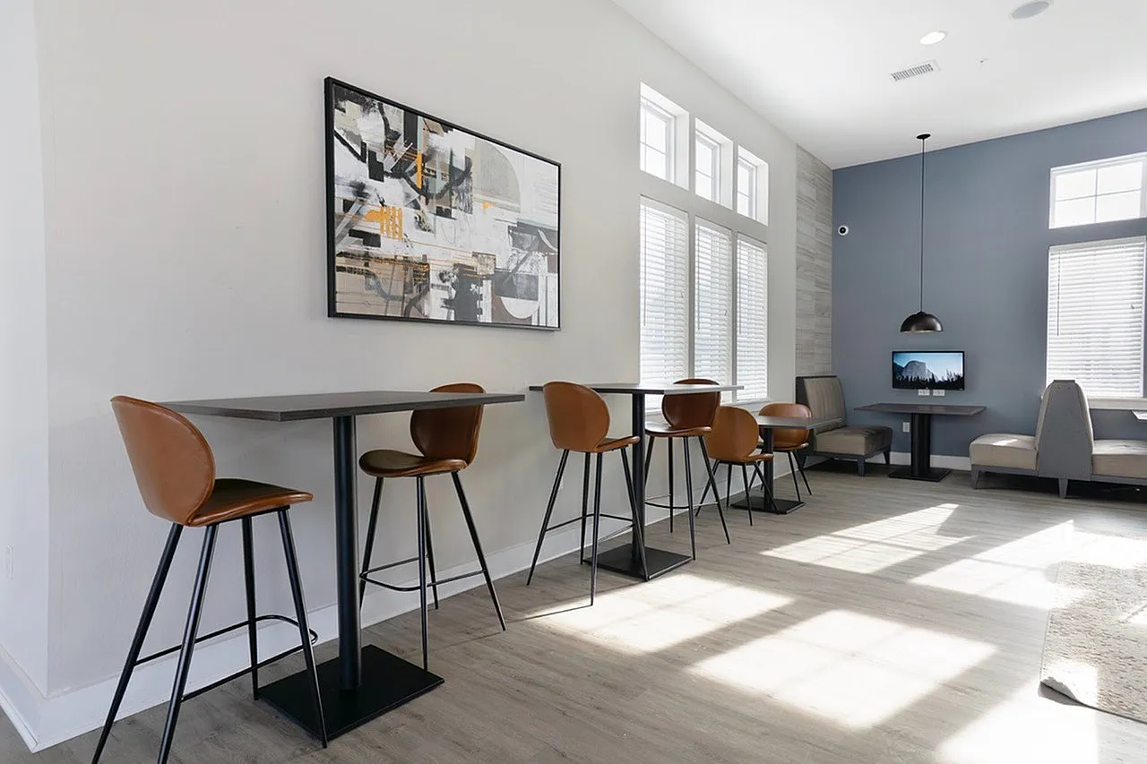 Modern communal space featuring sleek high tables with leather chairs, abstract artwork, and cozy seating under natural light.
