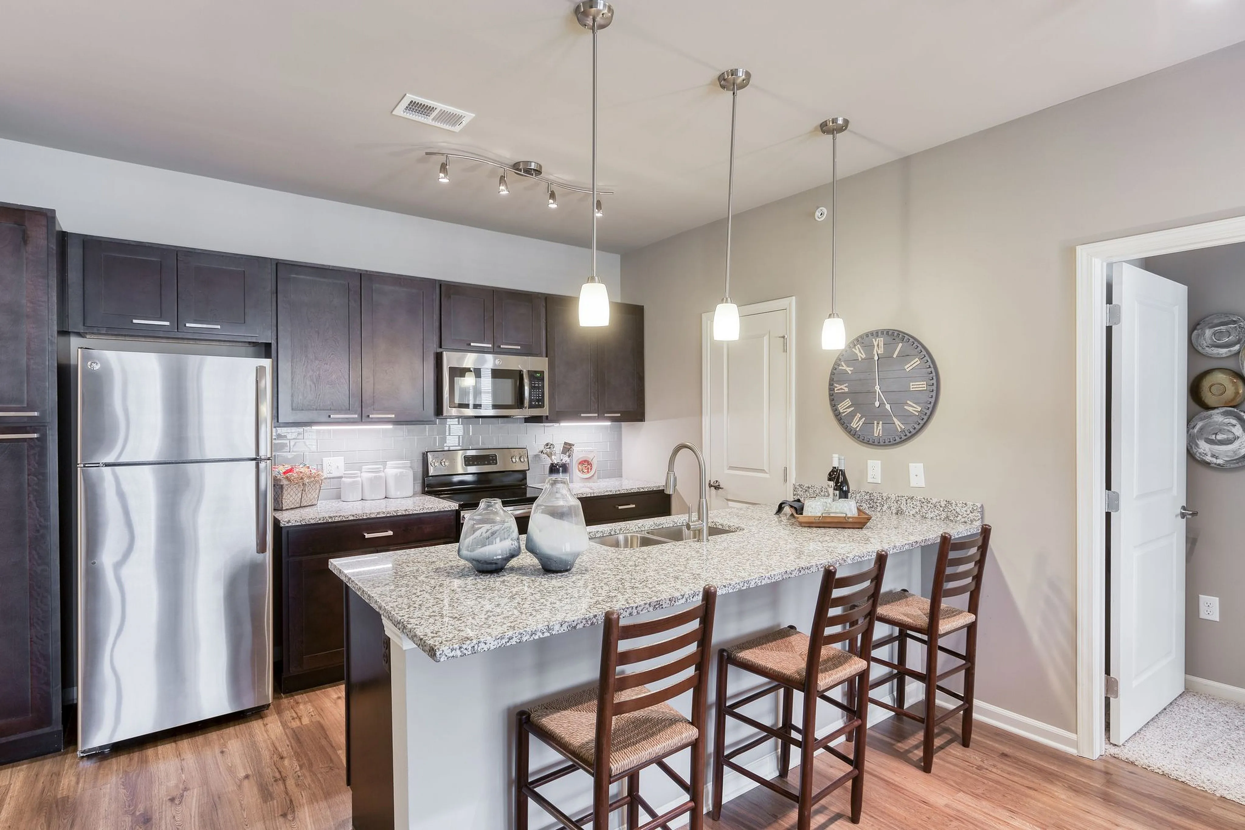 Modern kitchen with dark wood cabinets, granite countertops, stainless steel appliances, and stylish pendant lighting.