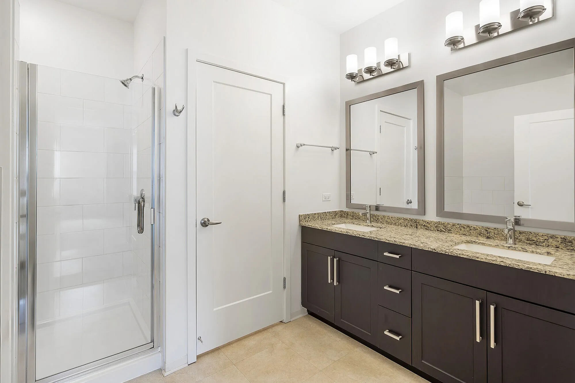 Elegant bathroom featuring a sleek glass shower, dual vanity with granite countertops, and modern lighting.