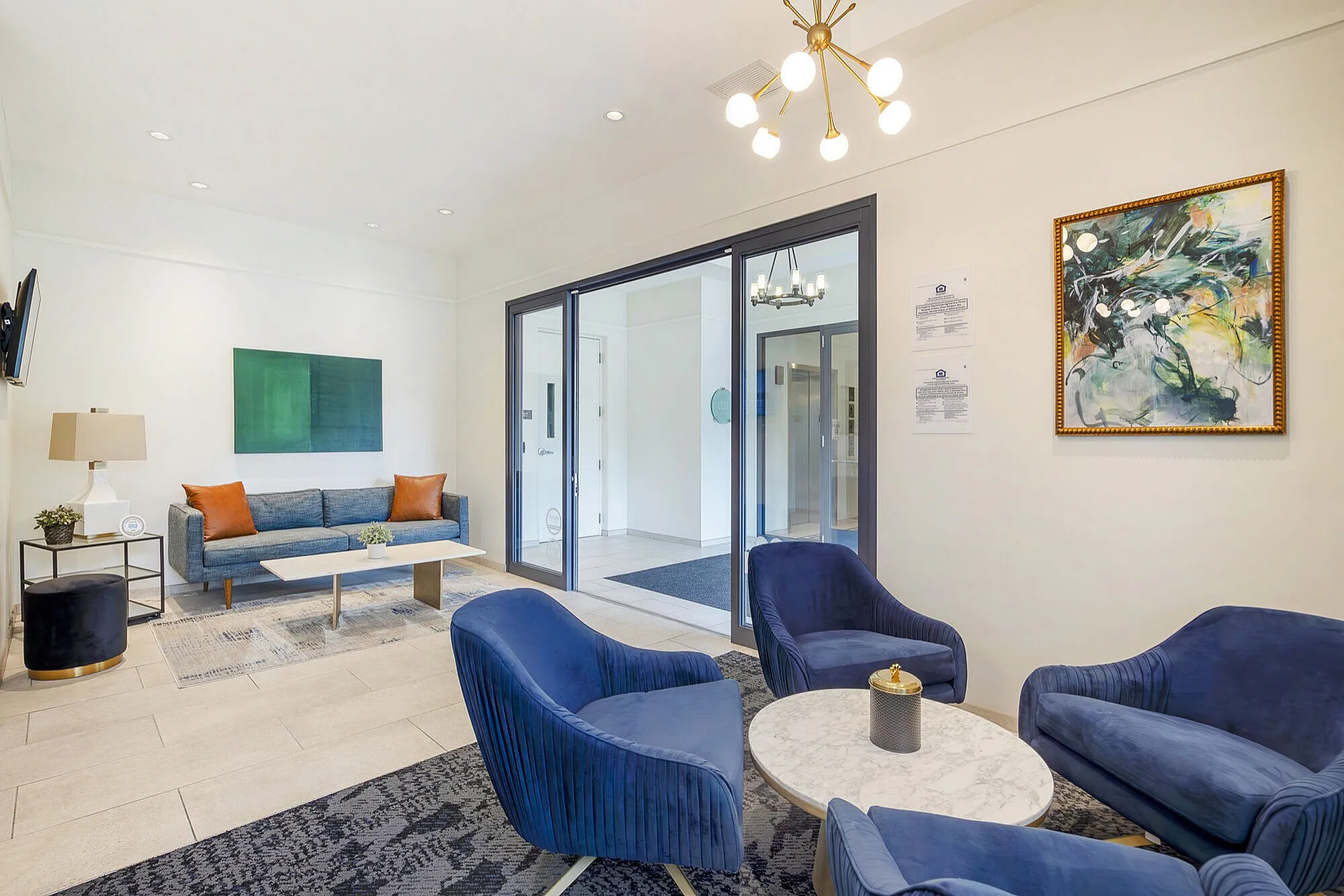 Modern apartment lobby with stylish blue seating, contemporary art, and elegant lighting, offering a welcoming atmosphere.