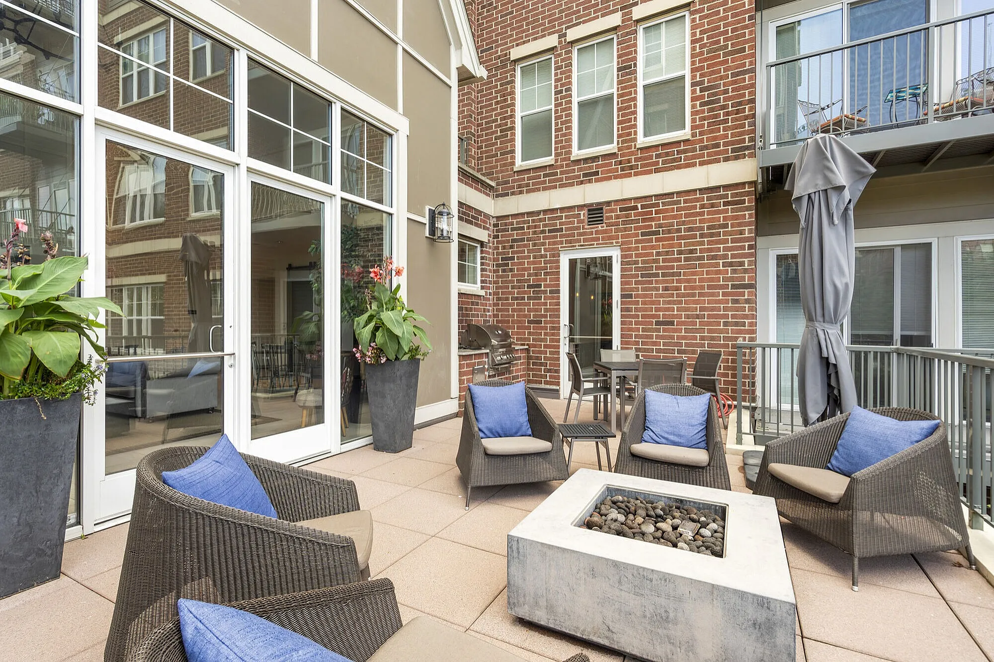 Chic outdoor patio with stylish wicker seating, vibrant plant accents, and a modern brick facade, offering a cozy and inviting retreat.
