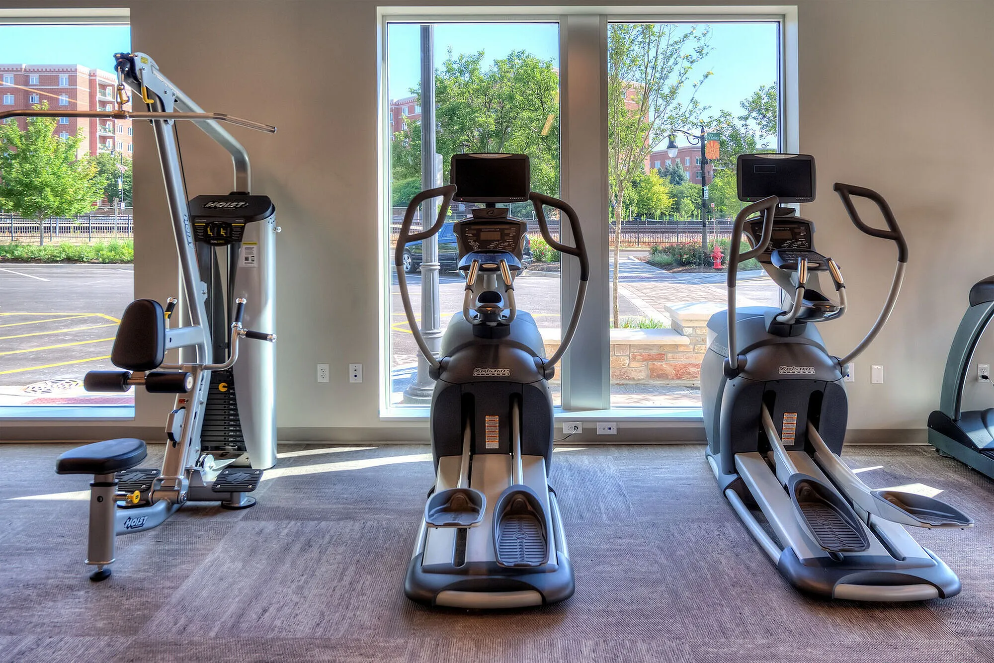Modern apartment gym featuring state-of-the-art exercise machines with large windows and abundant natural light.