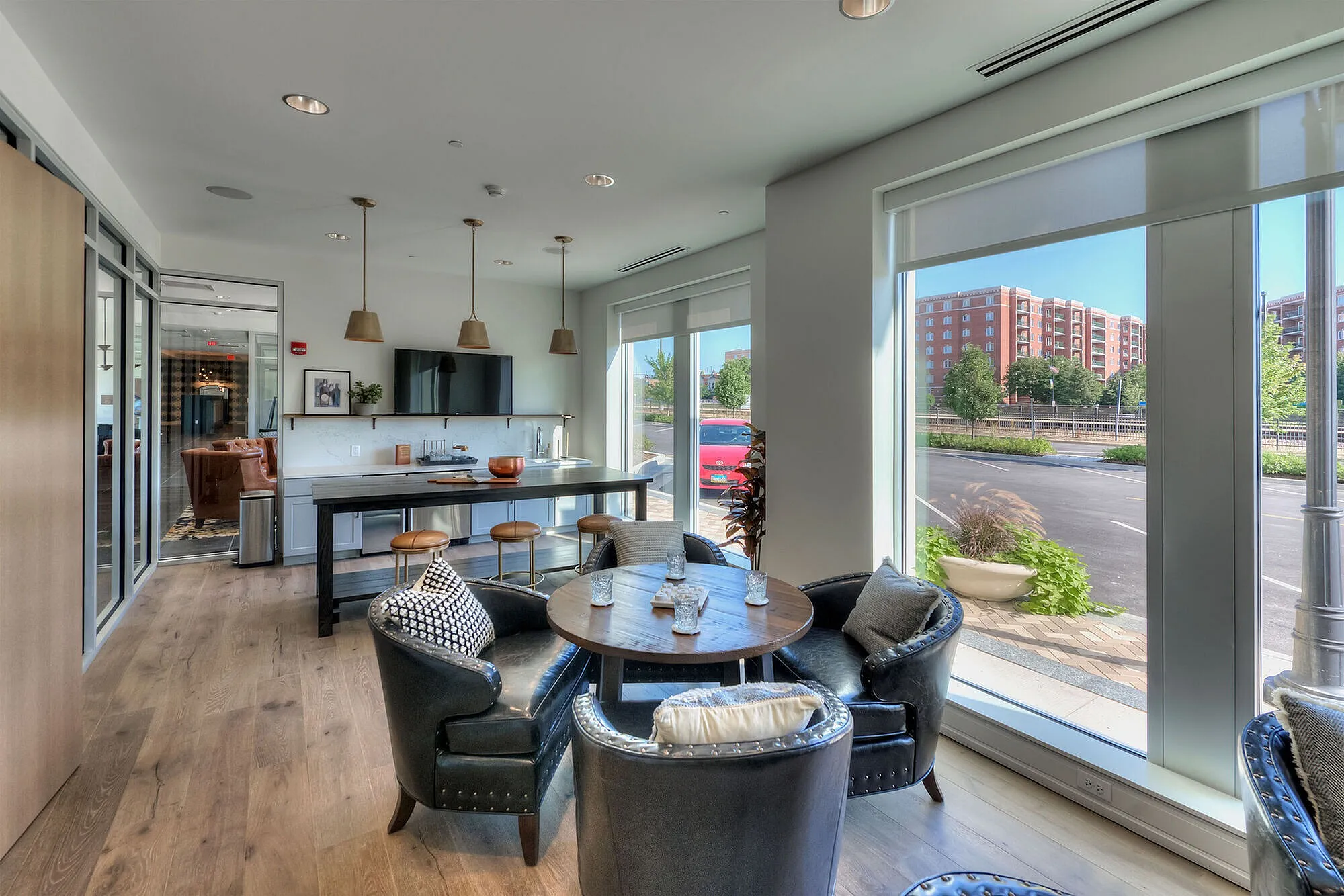 Modern apartment interior with sleek kitchen, cozy dining area featuring leather chairs, and large windows offering an expansive city view.