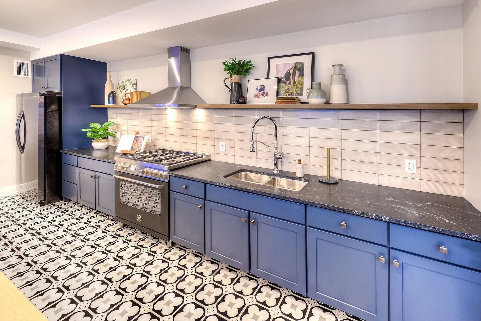 Chic modern kitchen with striking patterned flooring, sleek navy cabinets, and stainless steel appliances.